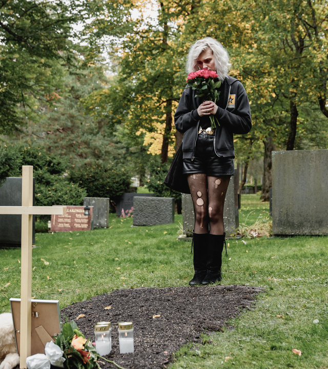 "Cryptid - Der Selbstversuch von Ester": Ester (Maja Johanna Englander) steht vor einem Grab. Darauf stehen Kerzen und ein Foto.