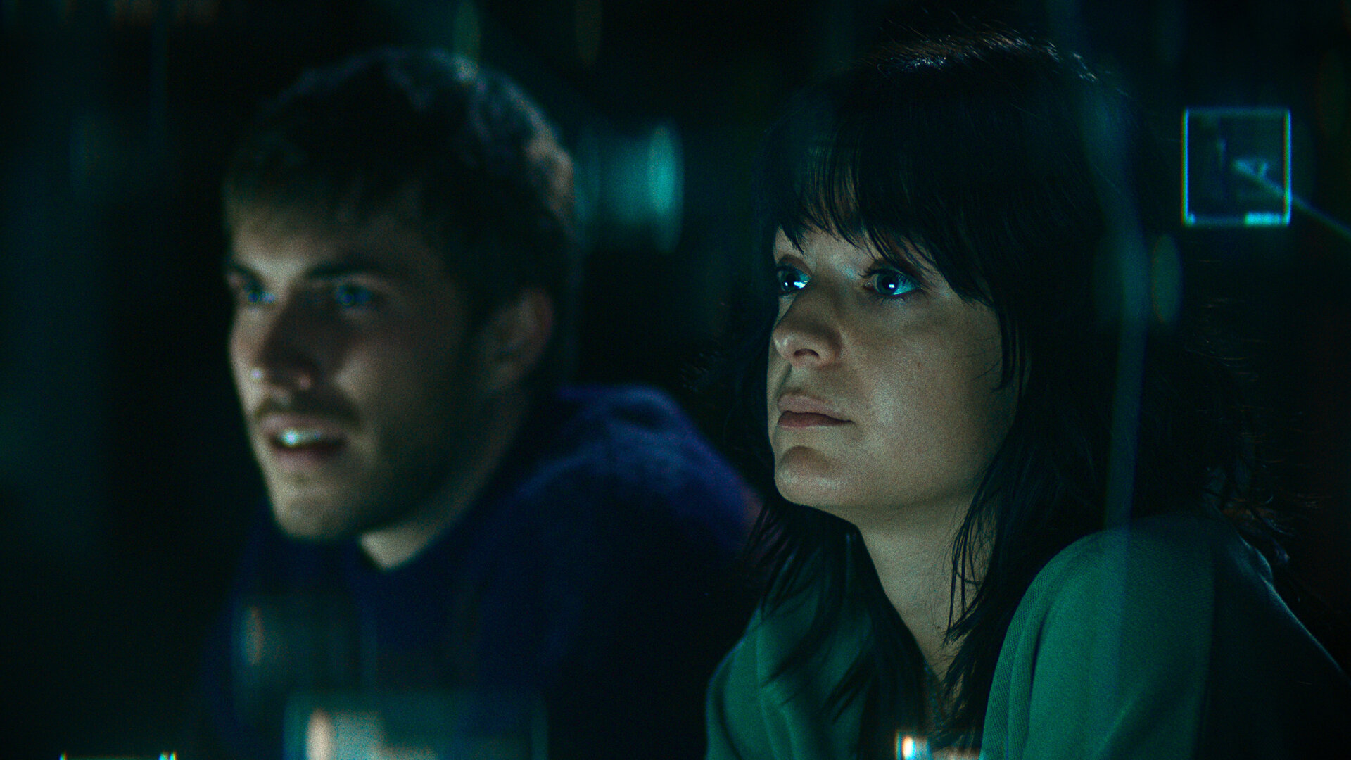 "The Kollective - Falsche Freunde": Aaron (Felix Mayr) und Delia (Céline Buckens) sitzen nebeneinander in einem dunklen Raum und beobachten etwas.