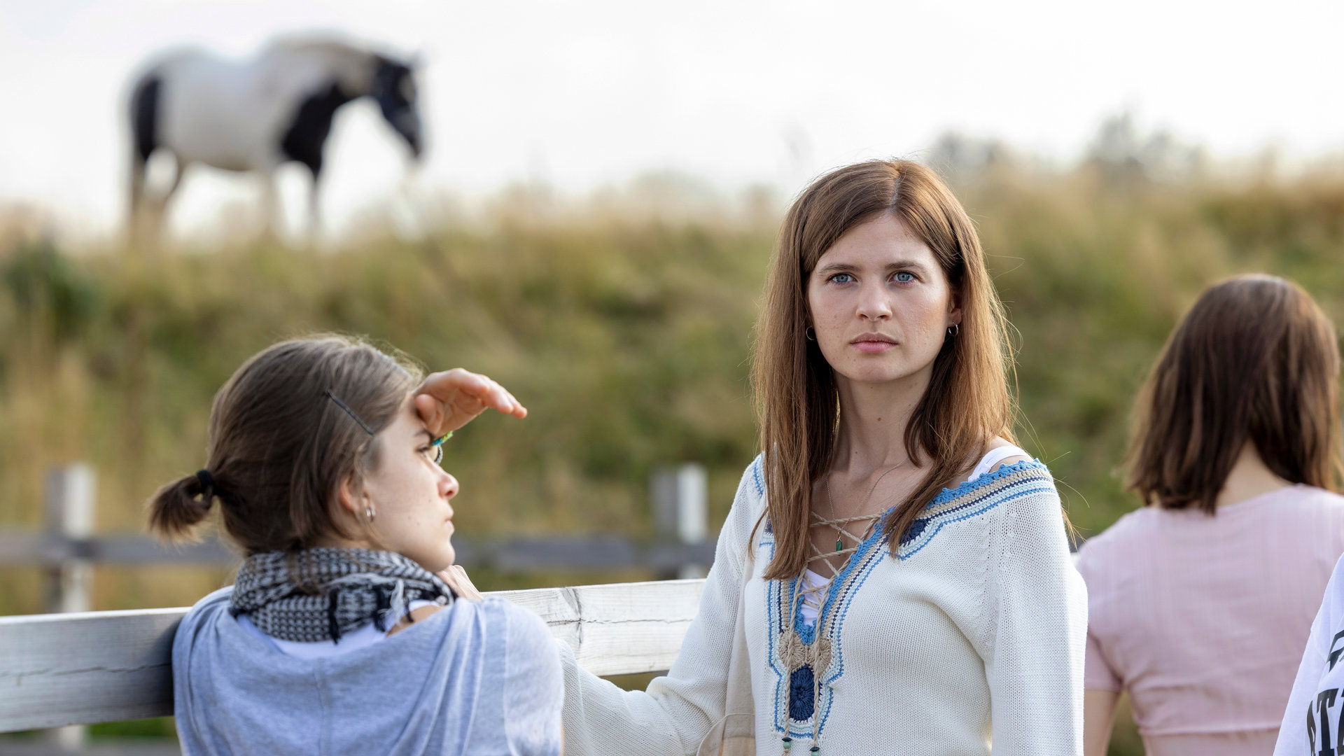 "Riding in Darkness - Die ganze Wahrheit": Agnes (Tehilla Blad) und (Victoria (Hanna Ardéhn) stehen vor einer Pferdekoppel. Agnes blickt zur Seite während sich Victoria sich umgedreht hat und in die Ferne blickt.