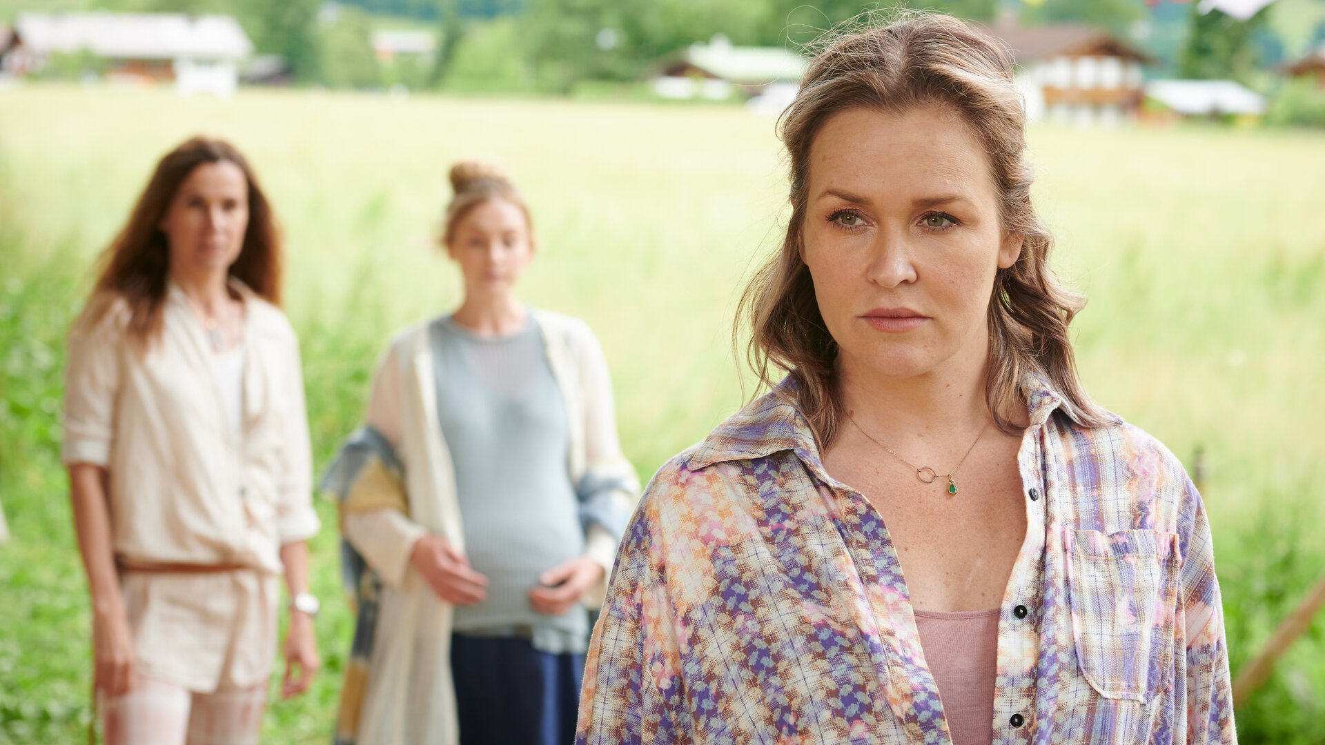 "Lena Lorenz - Freiheit": Auf einer Wiese steht Lena Lorenz (Judith Hoersch) im Vordergrund. Ihr Blick drückt Besorgnis aus. Im Hintergrund stehen Lilly Waldhauser (Teresa Klamert) und Marthe Gerber (Doris Schretzmayer).
