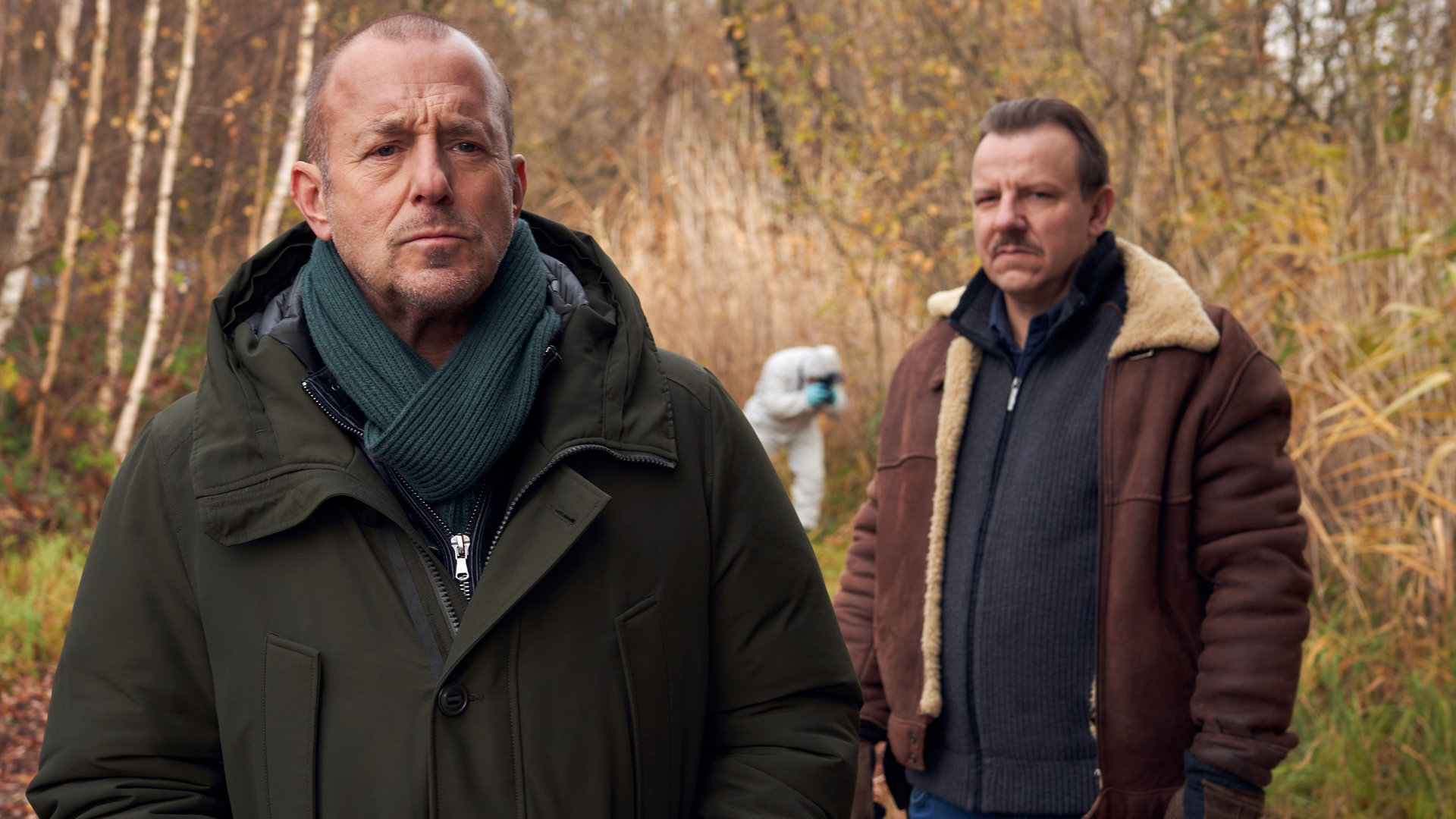 "Ingo Thiel - Ein Mädchen wird vermisst": Die beiden Ermittler Ingo Thiel (Heino Ferch) und Winni (Ronald Kukulies) stehen voreinander im Wald. Hinter ihnen ein Kollege von der Spurensicherung.