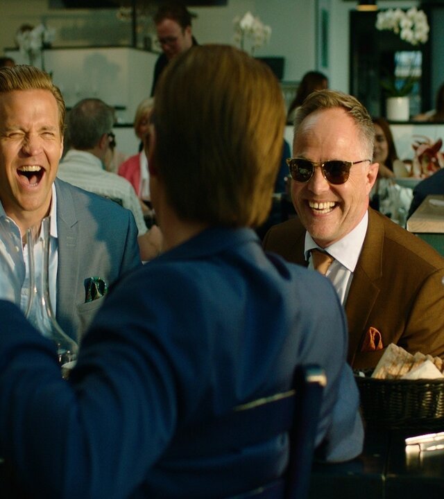 "Exit - Lazarus": Die Freunde Henrik (Tobias Santelmann), Jeppe (Jon Øigarden) und Adam (Simon J. Berger) sitzen lachend an einem Tisch in einem Restaurant.