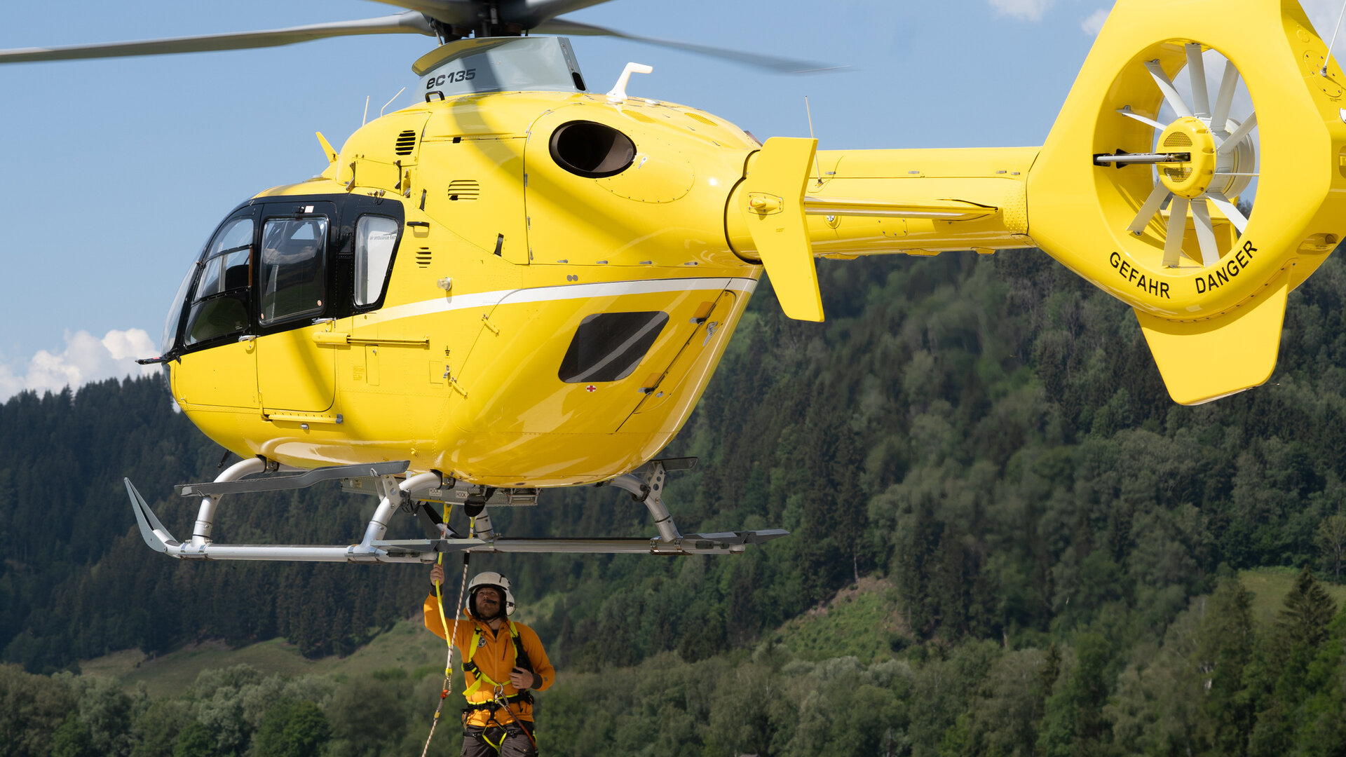 "Die Bergretter: Was wirklich zählt": Bergretter Markus (Sebastian Ströbel) steht unter dem Rettungshubschrauber, der nur wenige Meter über der Erde schwebt. Er befestigt ein Seil an der Unterseite des Hubschraubers.