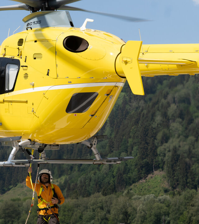 "Die Bergretter: Was wirklich zählt": Bergretter Markus (Sebastian Ströbel) steht unter dem Rettungshubschrauber, der nur wenige Meter über der Erde schwebt. Er befestigt ein Seil an der Unterseite des Hubschraubers.