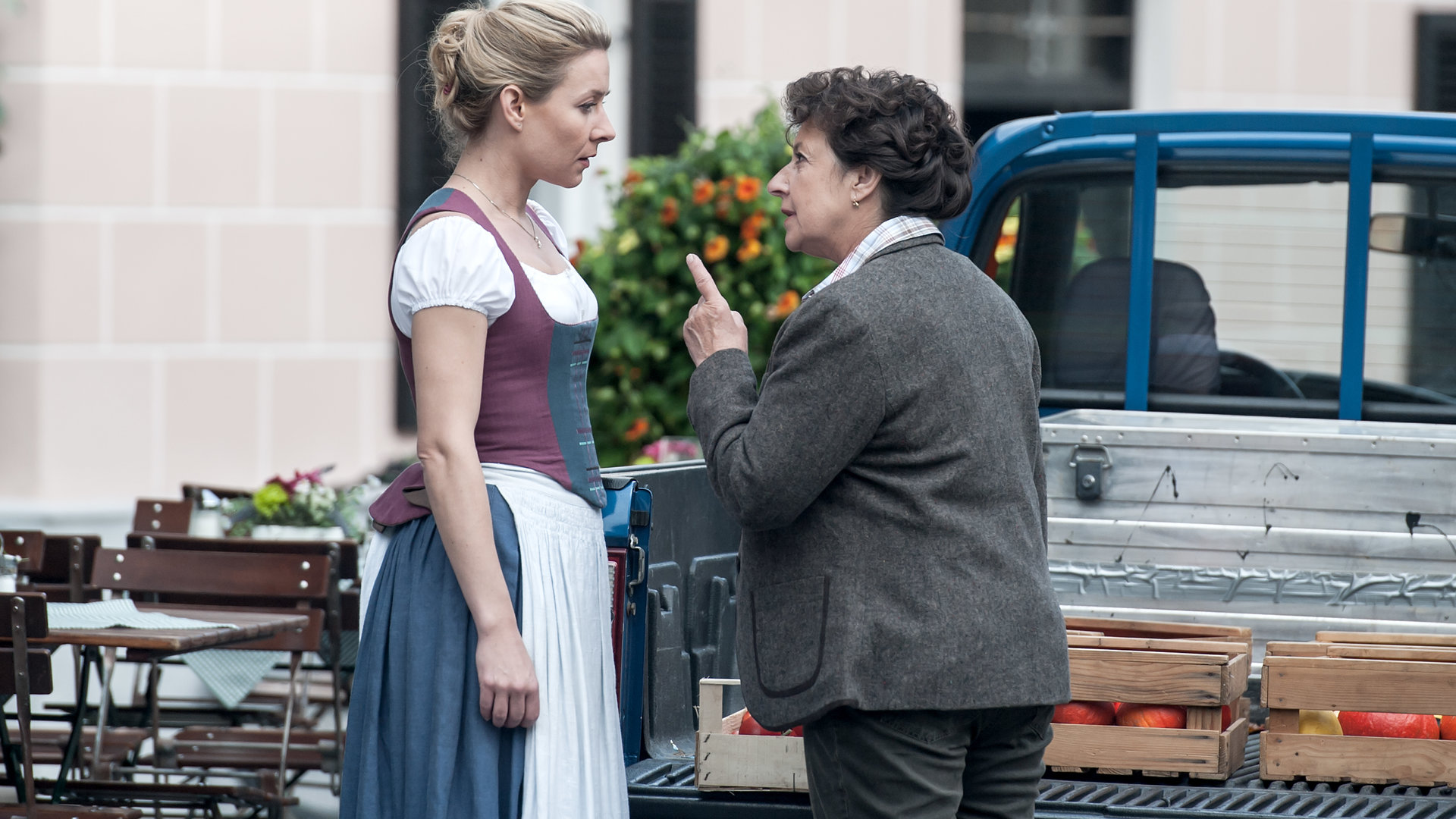 "Der Bergdoktor - Abschiede (1)": Lisbeth Gruber (Monika Baumgartner) steht Susanne (Natalie O'Hara) vor einem Lokal direkt gegenüber. Lisbeth spricht eindringlich mit Susanne und hat ihren Zeigefinger dabei erhoben.