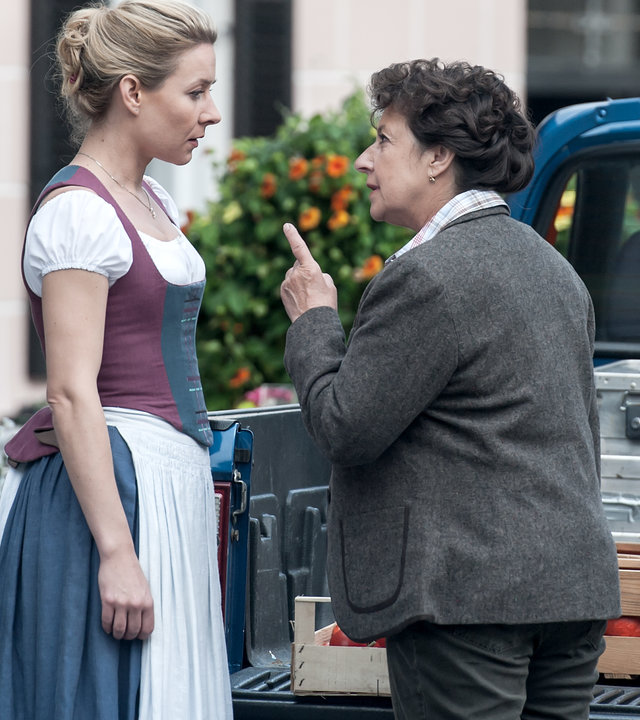 "Der Bergdoktor - Abschiede (1)": Lisbeth Gruber (Monika Baumgartner) steht Susanne (Natalie O'Hara) vor einem Lokal direkt gegenüber. Lisbeth spricht eindringlich mit Susanne und hat ihren Zeigefinger dabei erhoben.