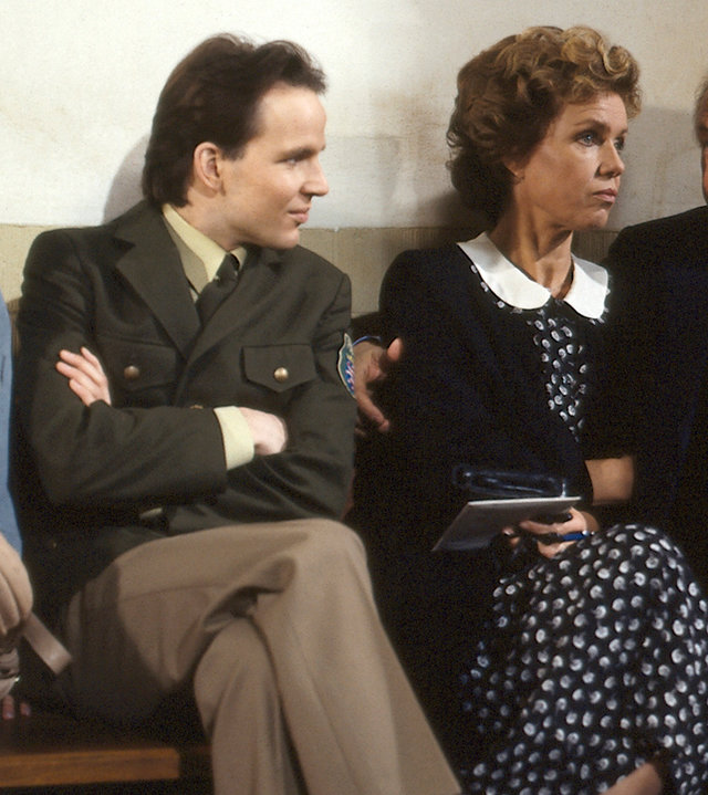 "Diese Drombusch - Der Prozeß": Tina Drombusch (Marion Kracht), Chris Drombusch (Mick Werup), Vera Drombusch (Witta Pohl) und Onkel Ludwig (Günter Strack) sitzen gemeinsam auf einer Bank vor einem Gerichtssaal.