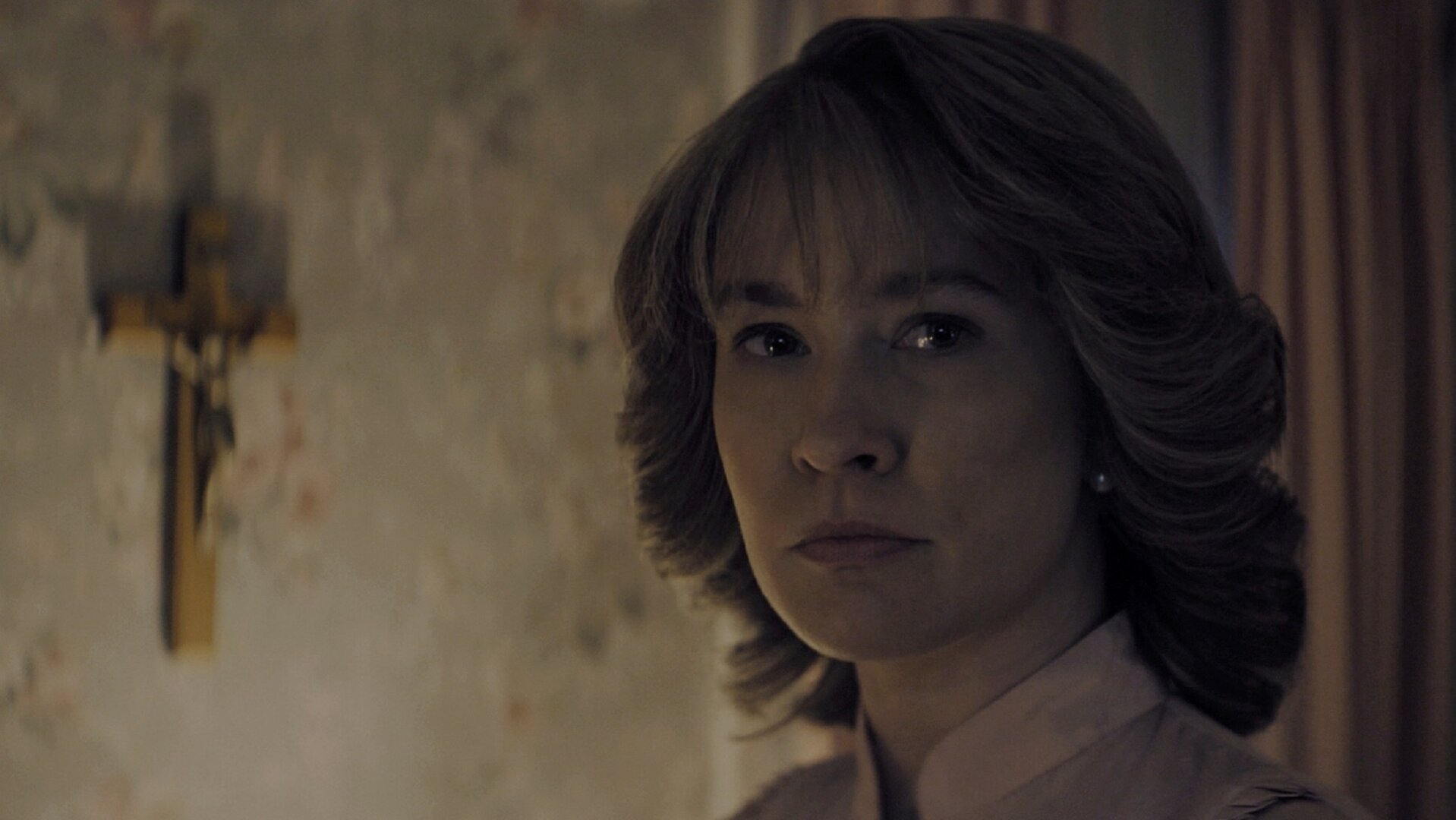 "Hysteria! - Leben aus dem Tod": Tracy (Anna Camp) steht in einem schwach beleuchteten Raum und blickt ernst zur Seite. Neben ihr hängt ein Kruzifix an der Wand.