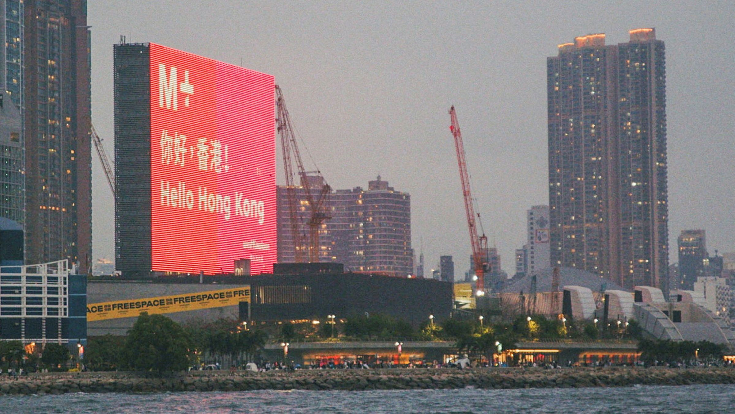 "Das M+ Museum und die Kunst in Hongkong": Das M+ Museum in der Abenddämmerung mit dem grossen LED-Screen.