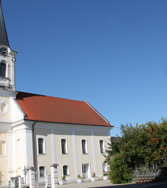 "Evangelischer Gottesdienst - Schau, es geht doch!": Die Pfarrkirche Oberwart im österreichischen Südburgenland ist außen hellgelb-weiß gestrichen, ihr Dach hat rote Ziegel. Der mit Schiefer bedeckte, eckige Kirchturm ragt in den wolkenlosen, blauen Himmel.