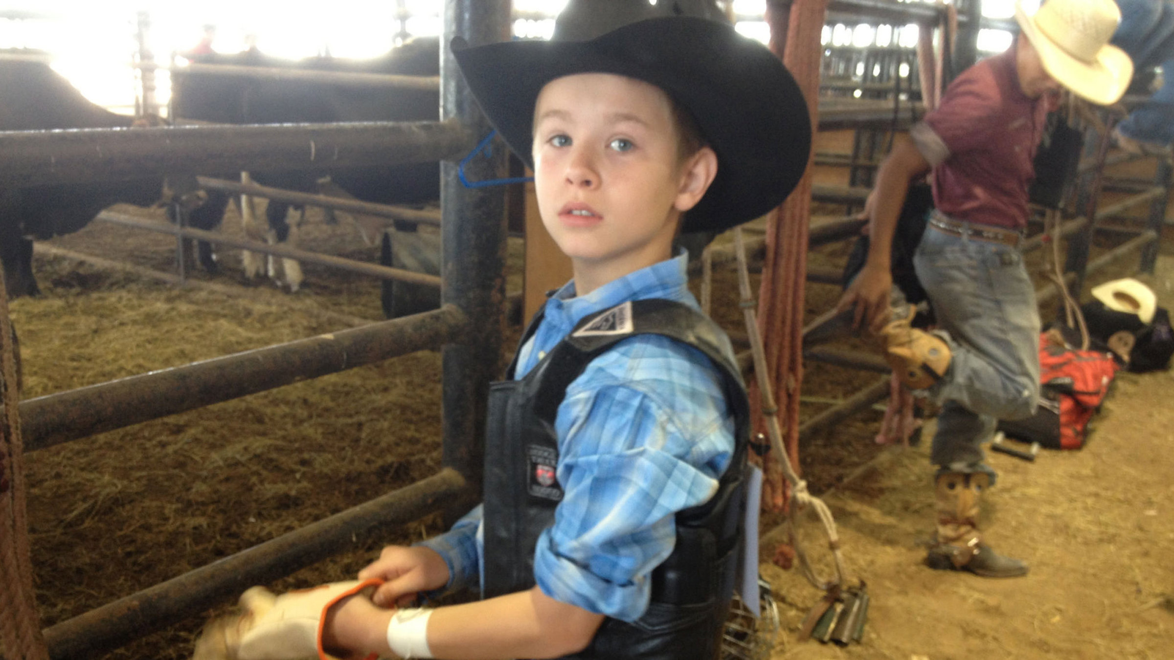 "Typisch Texas!": Junger Cowboy steht im Stall vor einem Zaun und zieht sich einen Handschuh an.