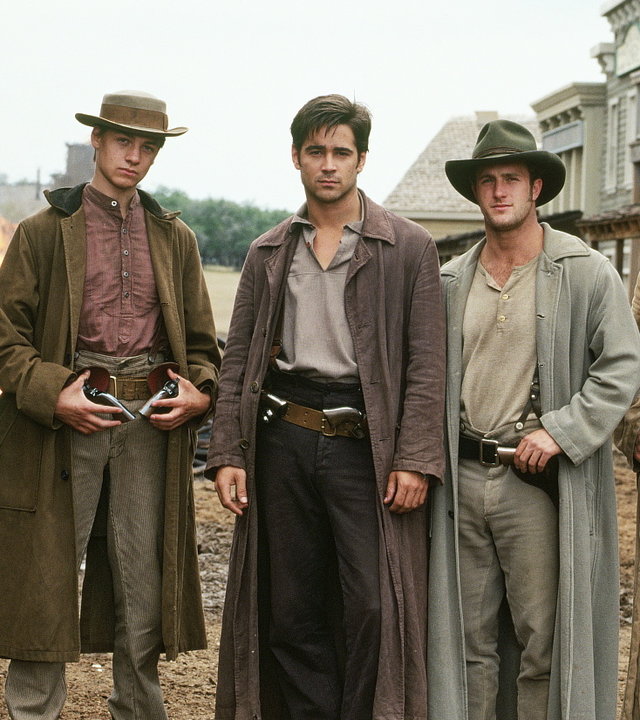 "American Outlaws" Fünf Famer stehen auf einer unbefestigten Straße nebeneinander. Im Hintergrund Häuser im Western-Stil. Die Männer tragen alle lange, naturfarbene Mäntel sowie Western-Hüte und Cowboy-Kleidung. Jesse James (Colin Farrell) steht in der Mitte. Alle blicken in Richtung Kamera.