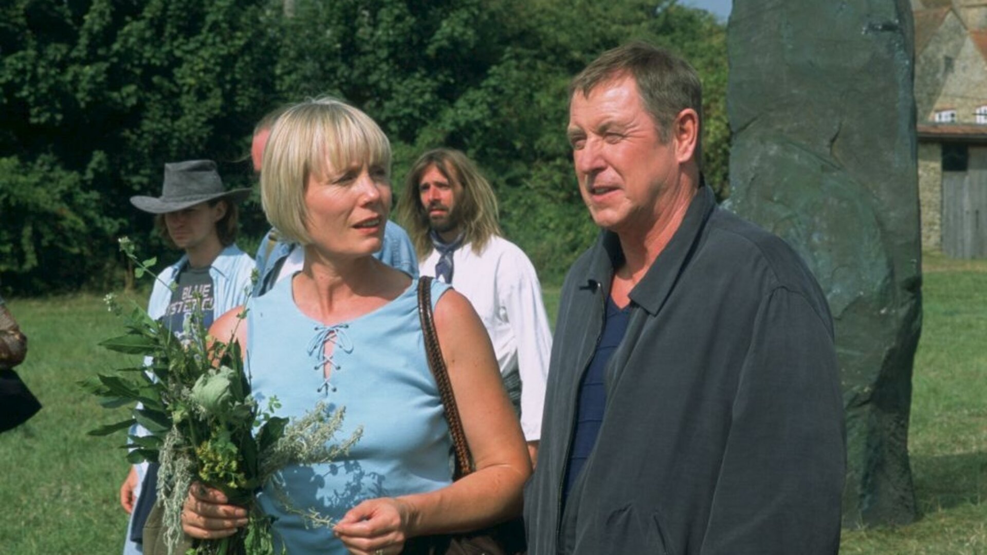 "Inspector Barnaby - Grab des Grauens": Joyce Barnaby (Jane Wymark) und DCI Tom Barnaby (John Nettles) stehen in einem Garten zusammen und unterhalten sich. Joyce hat einen Blumenstrauß in der Hand. Im Hintergrund sind weitere Personen zu erkennen.