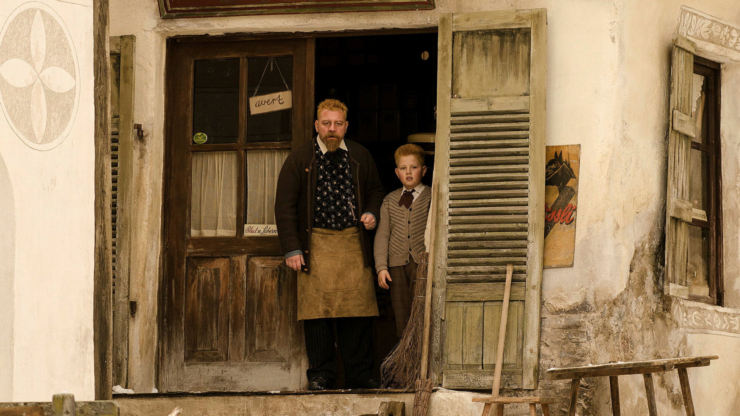 "Schellen-Ursli": Der reiche Ladenbesitzer Armon  (Leonardo Nigro) steht mit seinem Sohn Roman (Laurin Michael) im Eingang zum Laden.