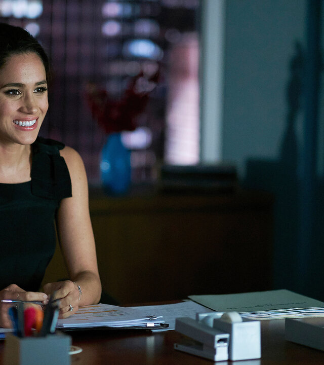 "Suits - Zwietracht": Rachel sitzt am Abend im dunklen Büro am Schreibtisch. Sie hält einen Stift in den Händen, die auf Dokumenten liegen. Sie lächelt und sieht erleichtert aus.
