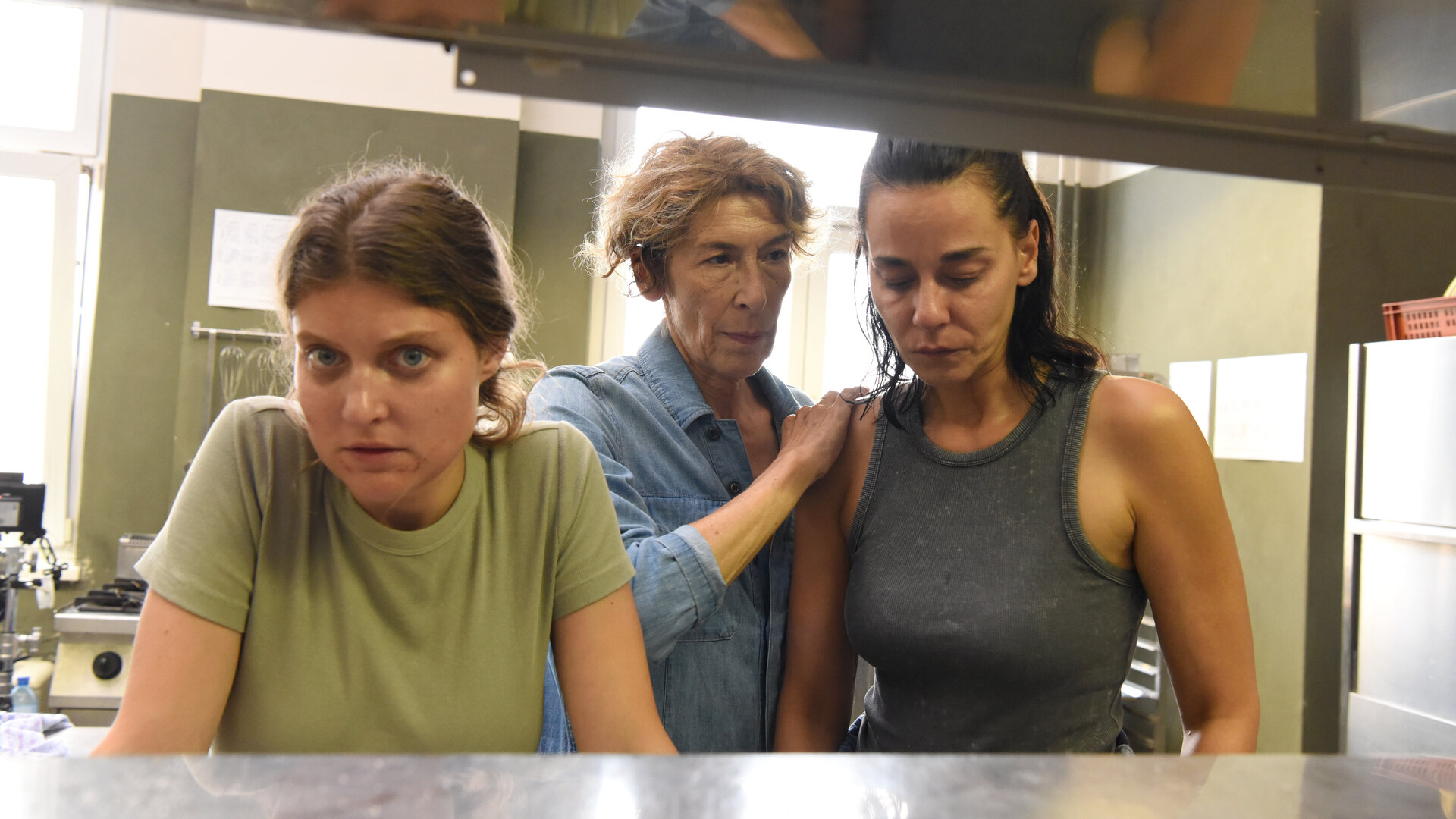 "Mama ist die Best(i)e Teil II": Gefängnisküche: Gloria (Adele Neuhauser) steht zwischen Henny (Lara Mandoki), die sich mit großen Augen an einer Theke abstützt, und Maria (Edita Malovčić, re), die betroffen vor sich blickt. Gloria hat die Hand beruhigend auf Marias Schulter gelegt. Im Hinter- und Vordergrund sind stählerne Verkleidungen zu sehen.