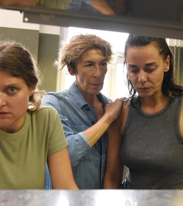 "Mama ist die Best(i)e Teil II": Gefängnisküche: Gloria (Adele Neuhauser) steht zwischen Henny (Lara Mandoki), die sich mit großen Augen an einer Theke abstützt, und Maria (Edita Malovčić, re), die betroffen vor sich blickt. Gloria hat die Hand beruhigend auf Marias Schulter gelegt. Im Hinter- und Vordergrund sind stählerne Verkleidungen zu sehen.