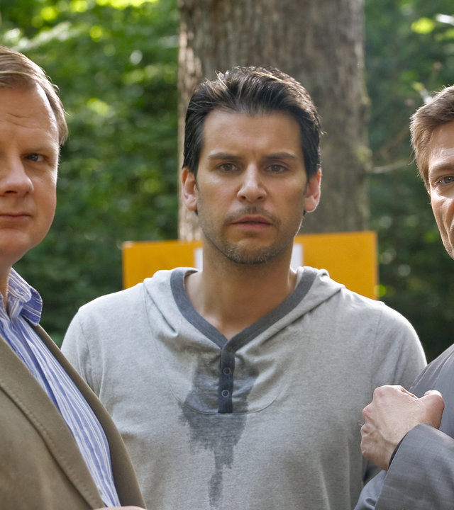 "Die Rosenheim-Cops: Ein Fall von Hochmut": Im Wald steht Kommissar Hartl (Michael A. Grimm) neben  Kletterkursteilnehmer Lindmayr (Florian Odendahl) und dem Kollegen Hansen (Igor Jeftic).