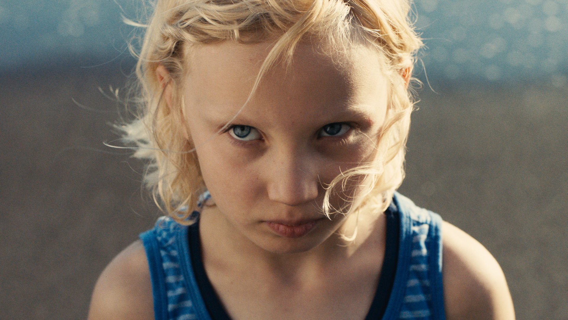 "Die Tochter":  Luca (Helena Zengel) in einem ärmellosen T-Shirt steht am Strand und schaut mit ernstem Blick nach oben.