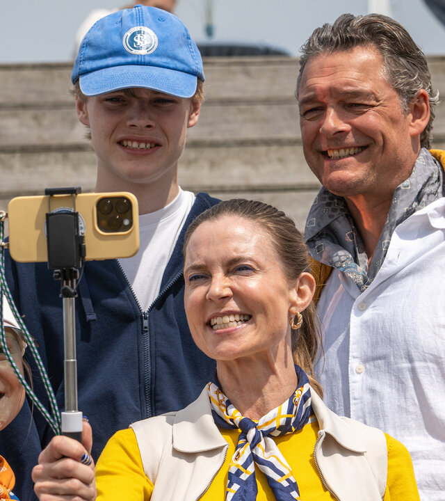 "Dan Sommerdahl - Tödliche Idylle: Tödlicher Ehrgeiz": Louise Busck (Camilla Gottlieb) nimmt mit ihren Kindern Frida (Rebekka Phillipson) und Karl (Mattias Brinch Nielsen) sowie ihrem Ehemann Jannik (Peter Reichhardt) auf einer Holztreppe im Hafen ein Foto auf. Louise hält ihr Smartphone in einem Selfiestick, alle lächeln in die Kamera.
