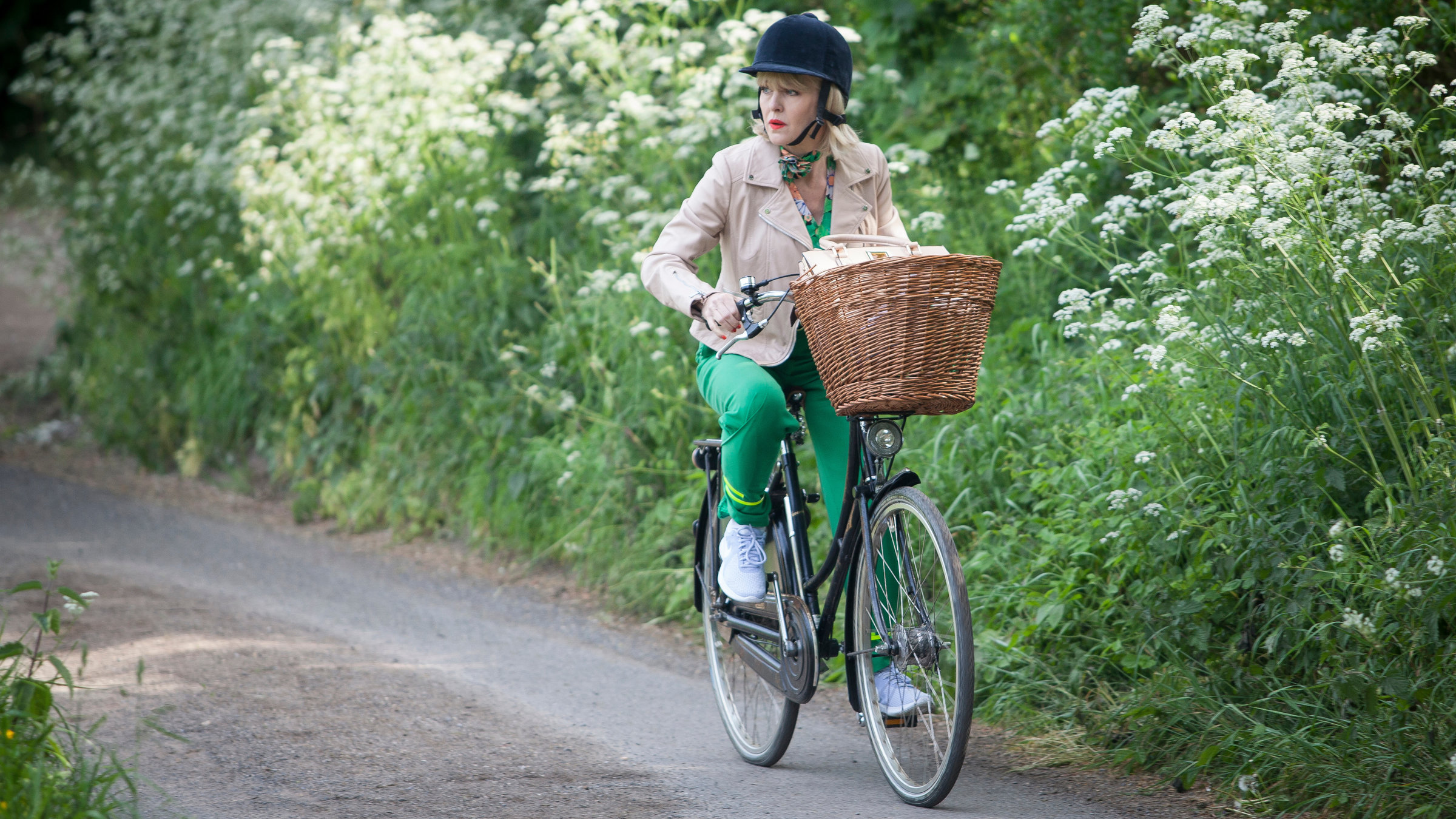 "Agatha Raisin - Der tote Gutsherr Teil 2": Agatha Raisin (Ashley Jensen) sitzt auf einem schwarzen Fahrrad und fährt einen Waldweg entlang.