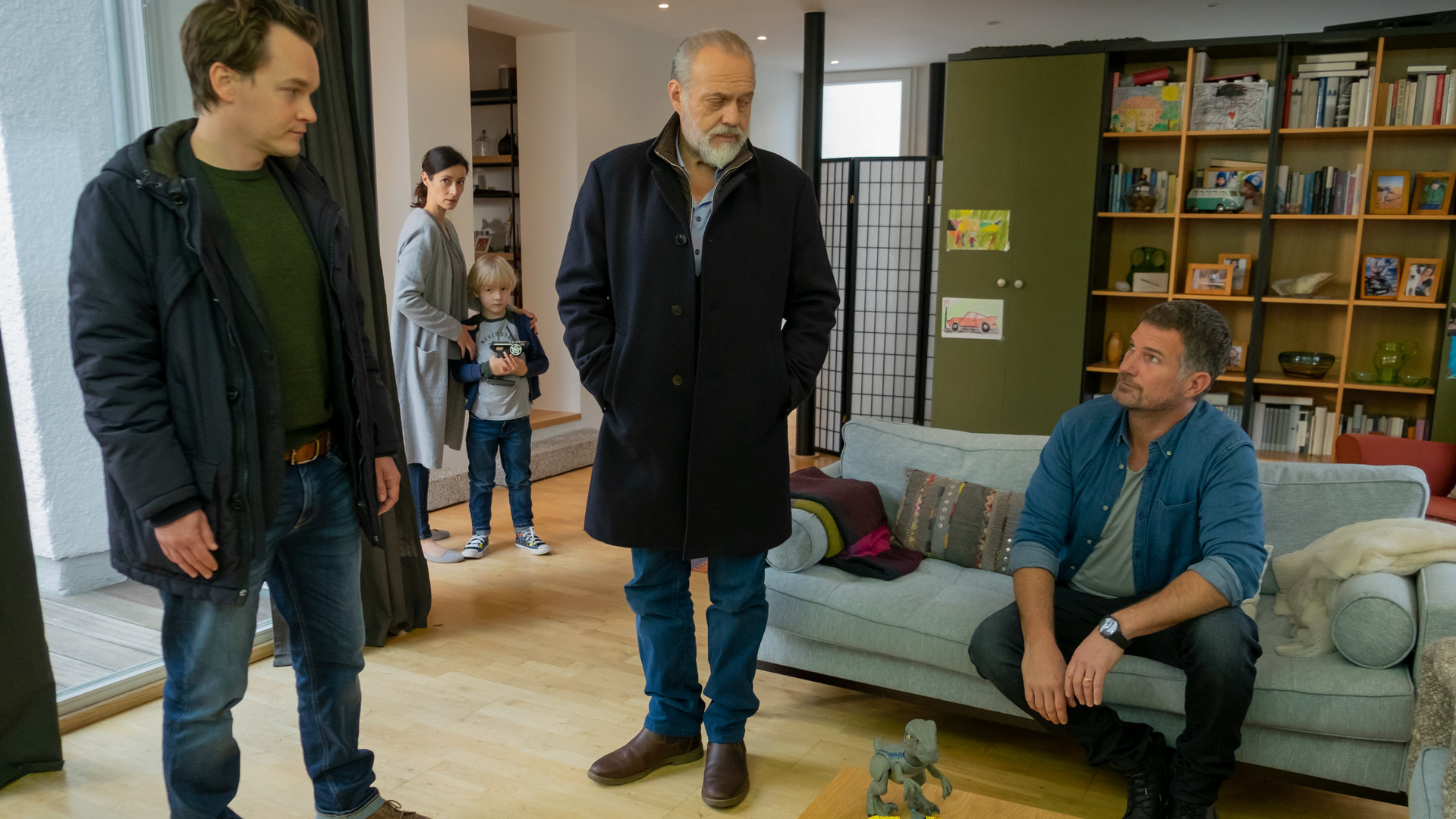 "Der Alte - Verantwortung": Tom Kupfer (Ludwig Blochberger) und Richard Voss (Jan-Gregor Kremp) stehen bei Alex Volkmann (Simon Böer) im Wohnzimmer, um sich mit ihm zu unterhalten. Marie Volkmann (Katrin Anne Heß) steht im Hintergrund bei ihrem kleinen Kind Max (Komparse).