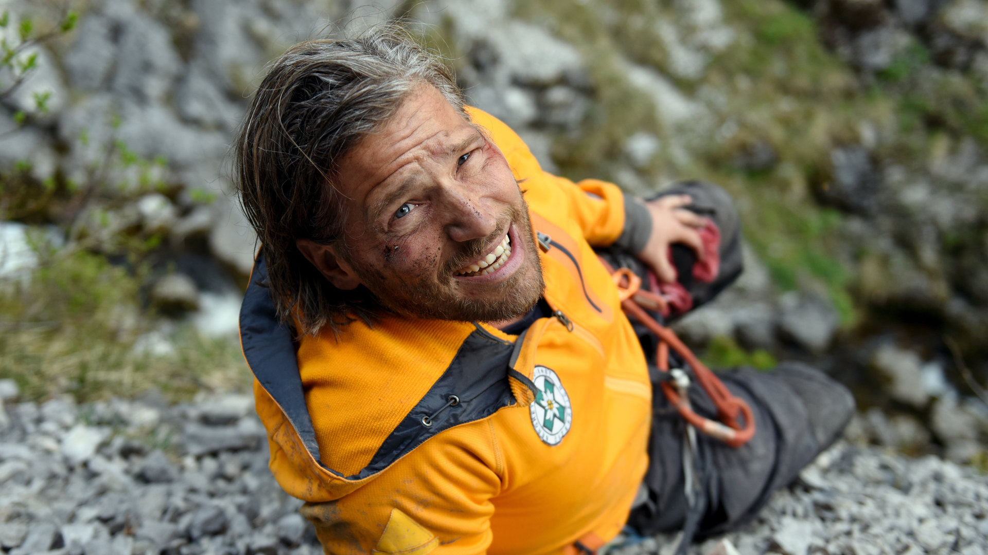 "Die Bergretter - Um jeden Preis (2)": Auf Steingeröll liegt Markus (Sebastian Ströbel) mit schmerzverzerrtem Gesicht. Er hält sich mit einer Hand sein blutendes Bein, in der anderen Hand hält er ein Funkgerät.