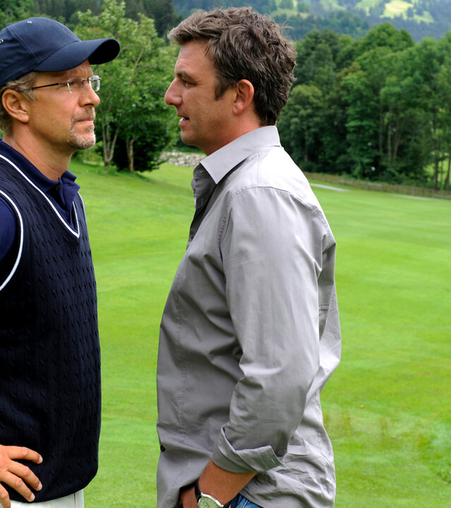 "Der Bergdoktor - Blindes Vertrauen": Der Bergdoktor Martin (Hans Sigl) und Prof. Thielen (Jochen Horst) stehen sich auf einem Golfplatz gegenüber. Martin hat seine Hände in den Hosentaschen und schaut Prof. Thielen prüfend an, der an Martin vorbei in die Ferne schaut.