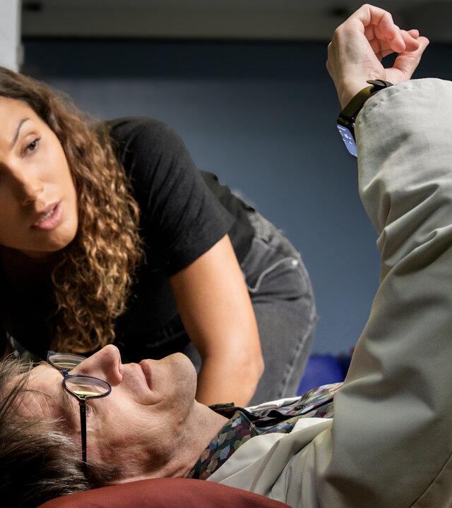 "SOKO Leipzig - Unsterblich": Kim Nowak (Amy Mußul) kniet neben dem liegenden Lorenz Rettig (Daniel Steiner) in dessen Labor auf dem Boden. Sie schauen beide auf die Smartwatch an seinem Handgelenk.