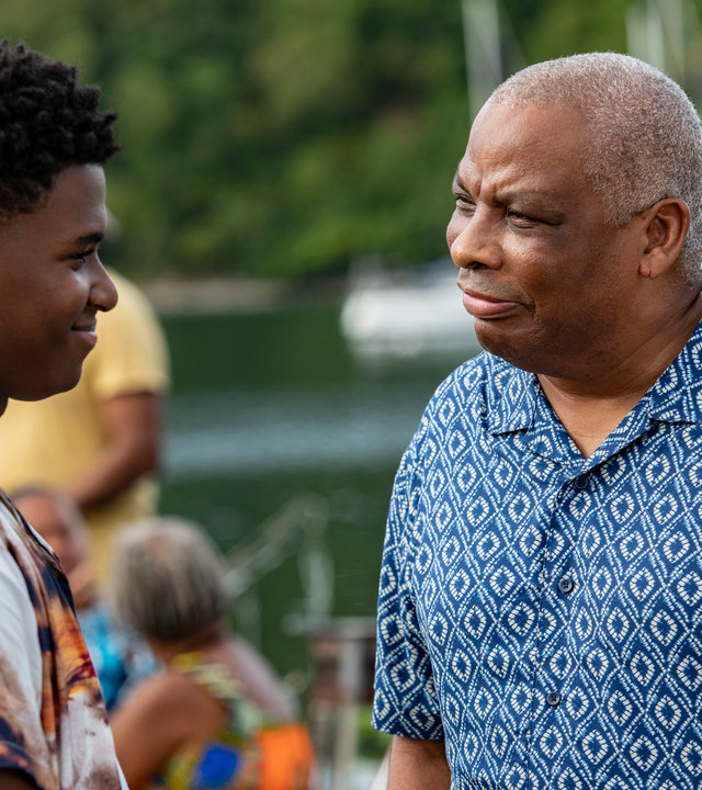 "Death in Paradise - Licht im Dunkeln": Marlon (Tahj Miles) und Commissioner Patterson (Don Warrington) stehen sich auf einem Pier gegenüber. Beide tragen bunte Freizeithemden und schauen sich aufrichtig an.