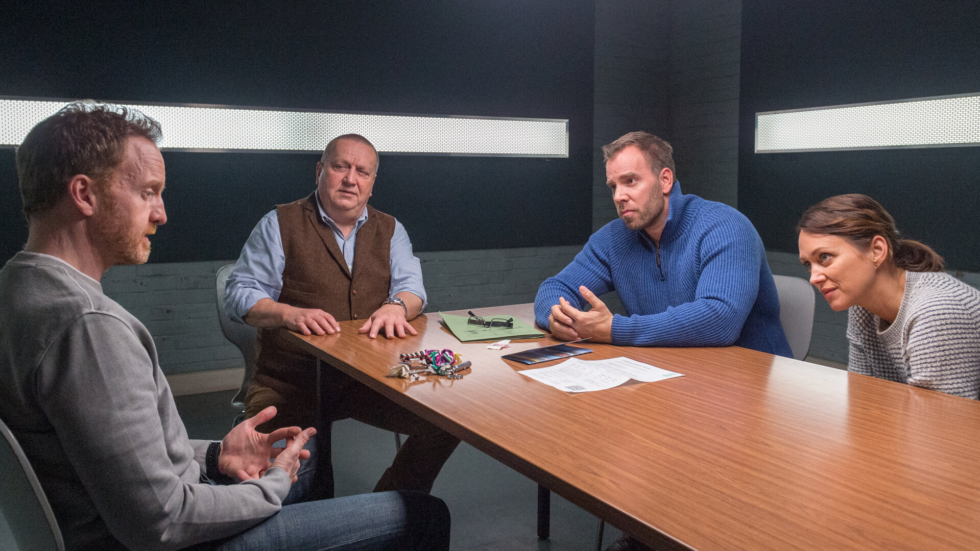 "SOKO Wismar – Täter Timmermann": Timmermann (Mathias Junge), in Zivil, wird von Jan Reuter (Udo Kroschwald), Lars Pöhlmann (Dominic Boeer) und Karoline Joost (Nike Fuhrmann) im Vernehmungsraum befragt. Vor Timmermann auf dem Tisch liegen ein Schlüsselbund und verschiedene Papiere.