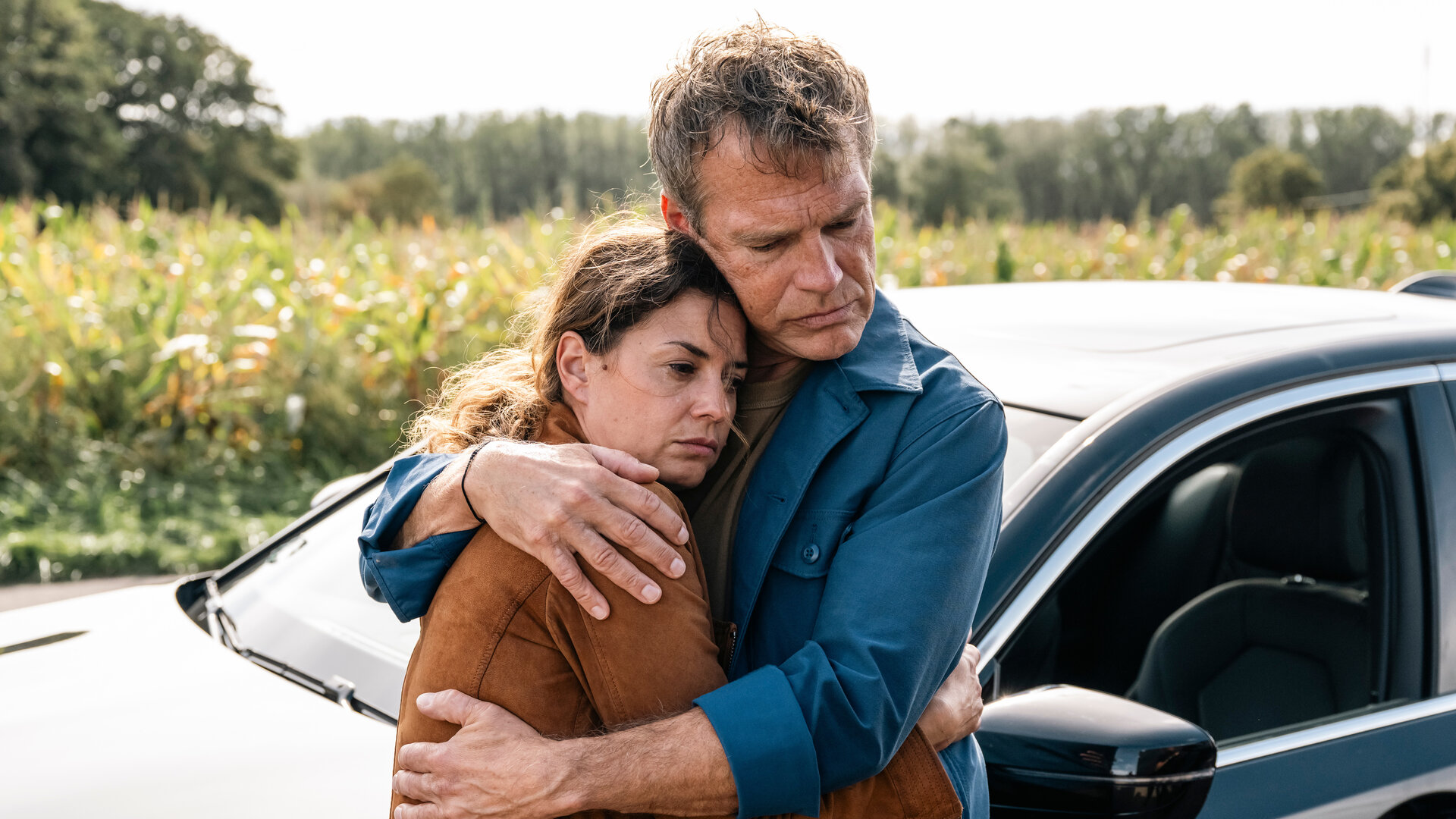 "SOKO Köln - Tödlicher Steinwurf": Matti Wagner (Pierre Besson) hält Lilly Funke (Tatjana Kästel) im Arm, die traurig nach unten sieht. Sie erwidert seine Umarmung. Die beiden stehen an einem Auto vor einer Grünfläche.