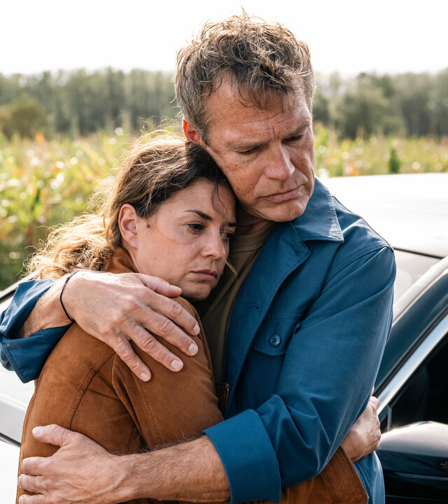 "SOKO Köln - Tödlicher Steinwurf": Matti Wagner (Pierre Besson) hält Lilly Funke (Tatjana Kästel) im Arm, die traurig nach unten sieht. Sie erwidert seine Umarmung. Die beiden stehen an einem Auto vor einer Grünfläche.