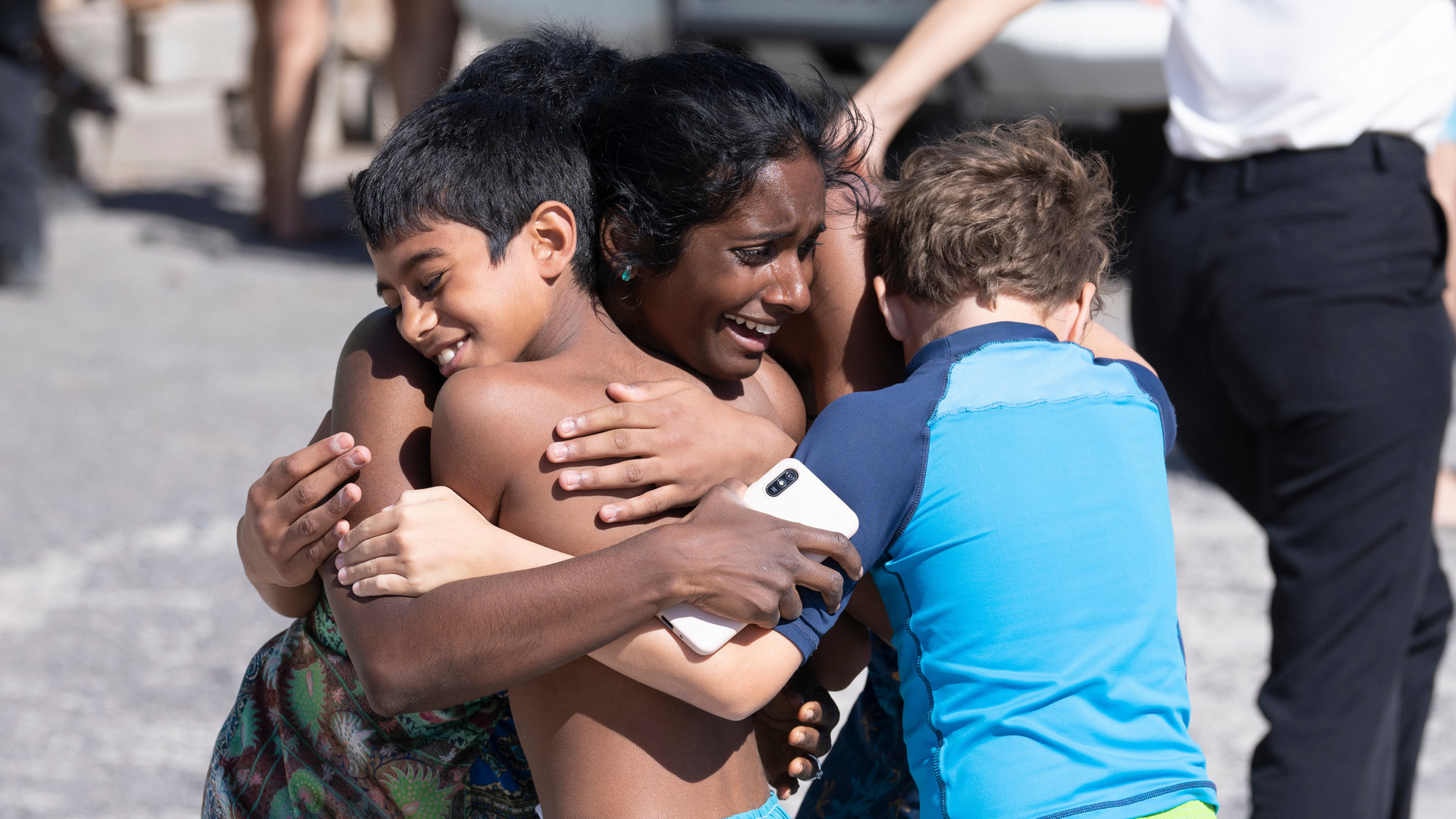 "Crossfire - Tod in der Sonne (3)": Abhi (Anneika Rose) hält lachend Jaypal (Arjun Subramanian) und Adam (Noah Leggott) in ihren Armen.