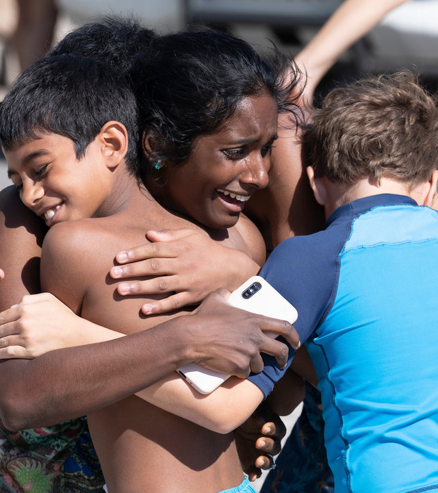"Crossfire - Tod in der Sonne (3)": Abhi (Anneika Rose) hält lachend Jaypal (Arjun Subramanian) und Adam (Noah Leggott) in ihren Armen.
