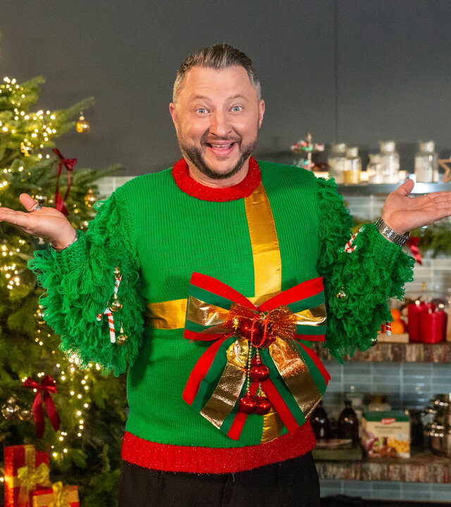 "besseresser: Die Tricks in Weihnachtsprodukten": Sebastian Lege trägt einen Weihnachtspulli mit großer Schleife und steht vor einem Weihnachtsbaum.