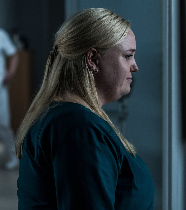 "Elvira - Erpresser gegen Erpresser": Elvira (Sara Klein) steht vor der Türe zu einem Krankenzimmer, in deren Glas sich ihr Profil spiegelt.