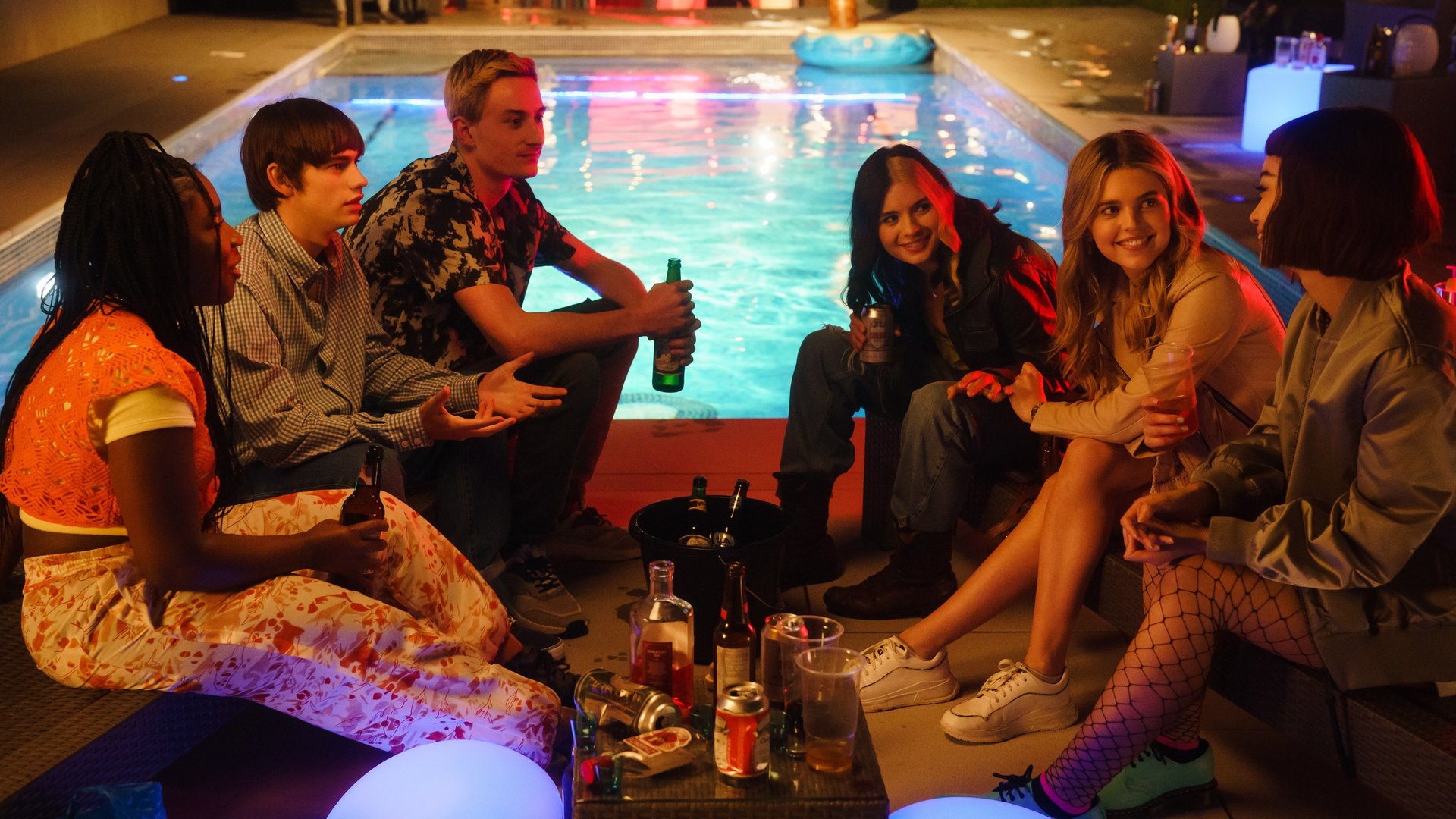 "Tell me everything: Schlaf": Neve (Lauryn Ajufo), Louis (Spike  E. Fearn), Jonny (Eden H. Davies), Regan (Tessa Lucille), Zia (Carla Woodcock) und Mei (Callina Liang) sitzen vor einem Pool auf dem Boden unterhalten sich ausgelassen und trinken Alkohol.