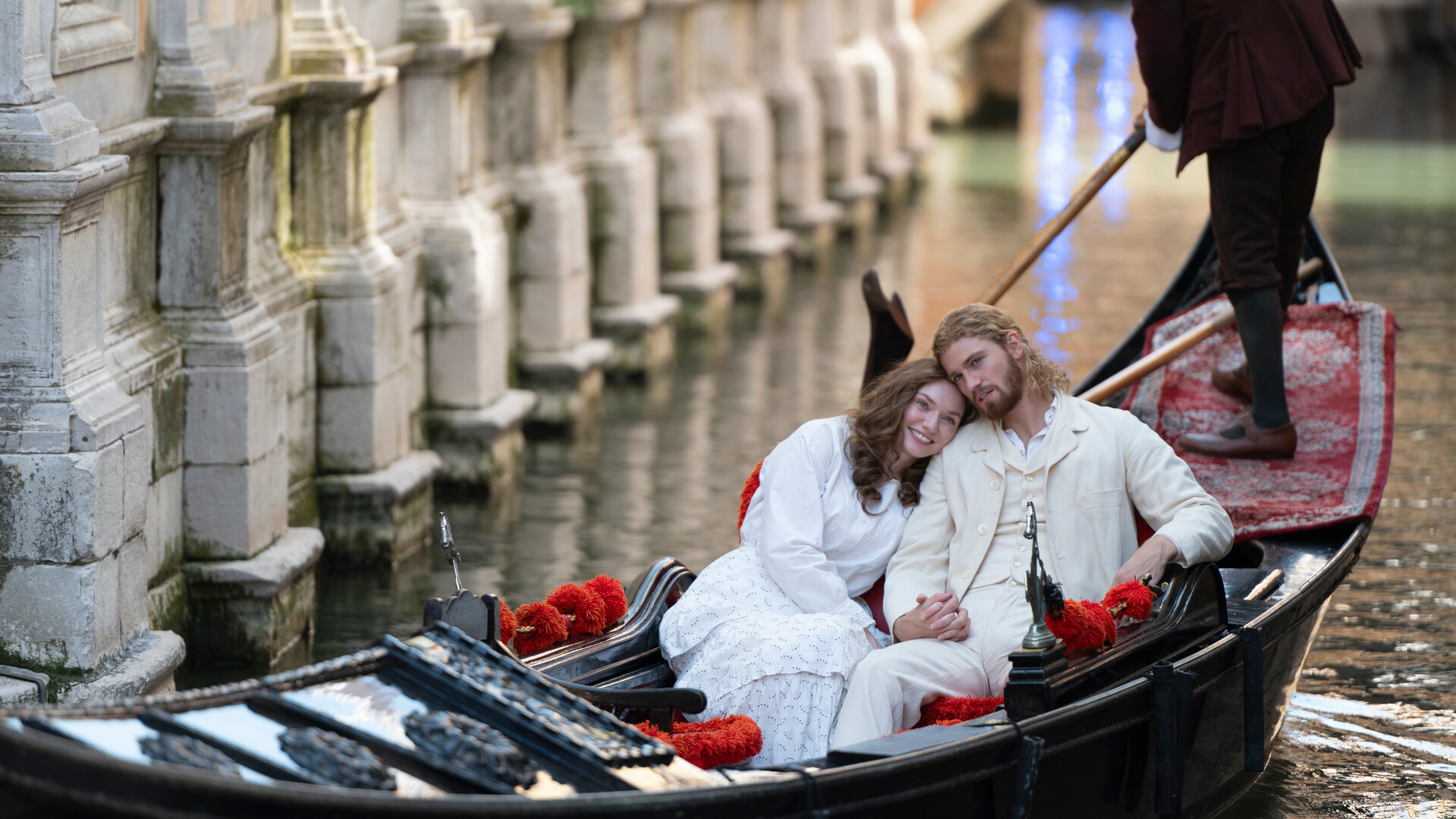 "The Forsytes - Familie verpflichtet: Heimliche Begierden": In einem Kanal in Venedig in einer Gondel: Luisa (Eleanor Tomlinson) lehnt ihren Kopf an Joylons (Danny Griffin) Schulter, beide sind weiß gekleidet. Hinter ihnen steht der Gondolière, der bis zur Hüfte zu erkennen ist.