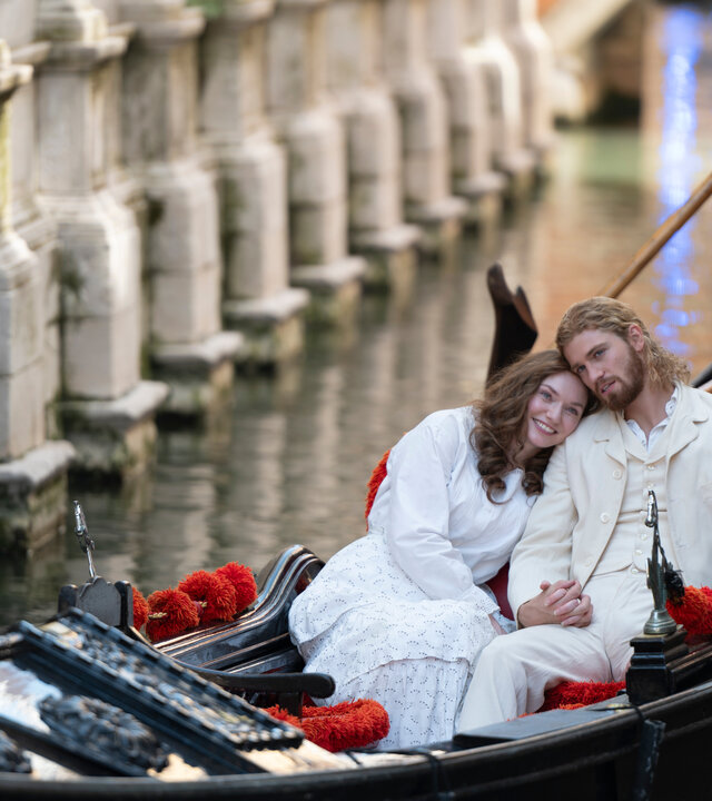 "The Forsytes - Familie verpflichtet: Heimliche Begierden": In einem Kanal in Venedig in einer Gondel: Luisa (Eleanor Tomlinson) lehnt ihren Kopf an Joylons (Danny Griffin) Schulter, beide sind weiß gekleidet. Hinter ihnen steht der Gondolière, der bis zur Hüfte zu erkennen ist.