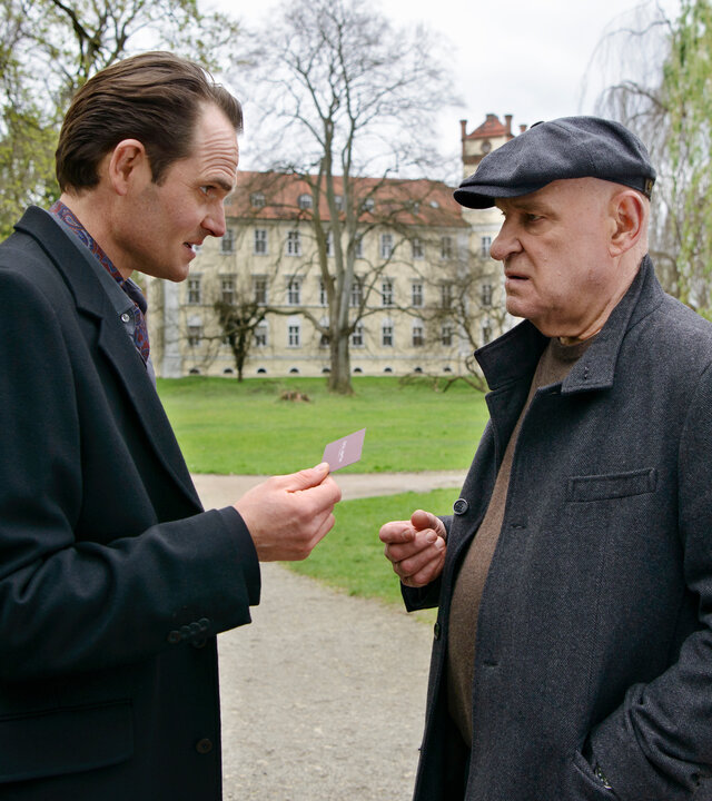 "Spreewaldkrimi - Böses muss mit Bösem enden": Kriminalrat a.D. Krüger (Christian Redl) und Prof. Levi A. Than (Fabian Hinrichs) unterhalten sich in einem Park. Prof. Than überreicht Krüger seine Visitenkarte.