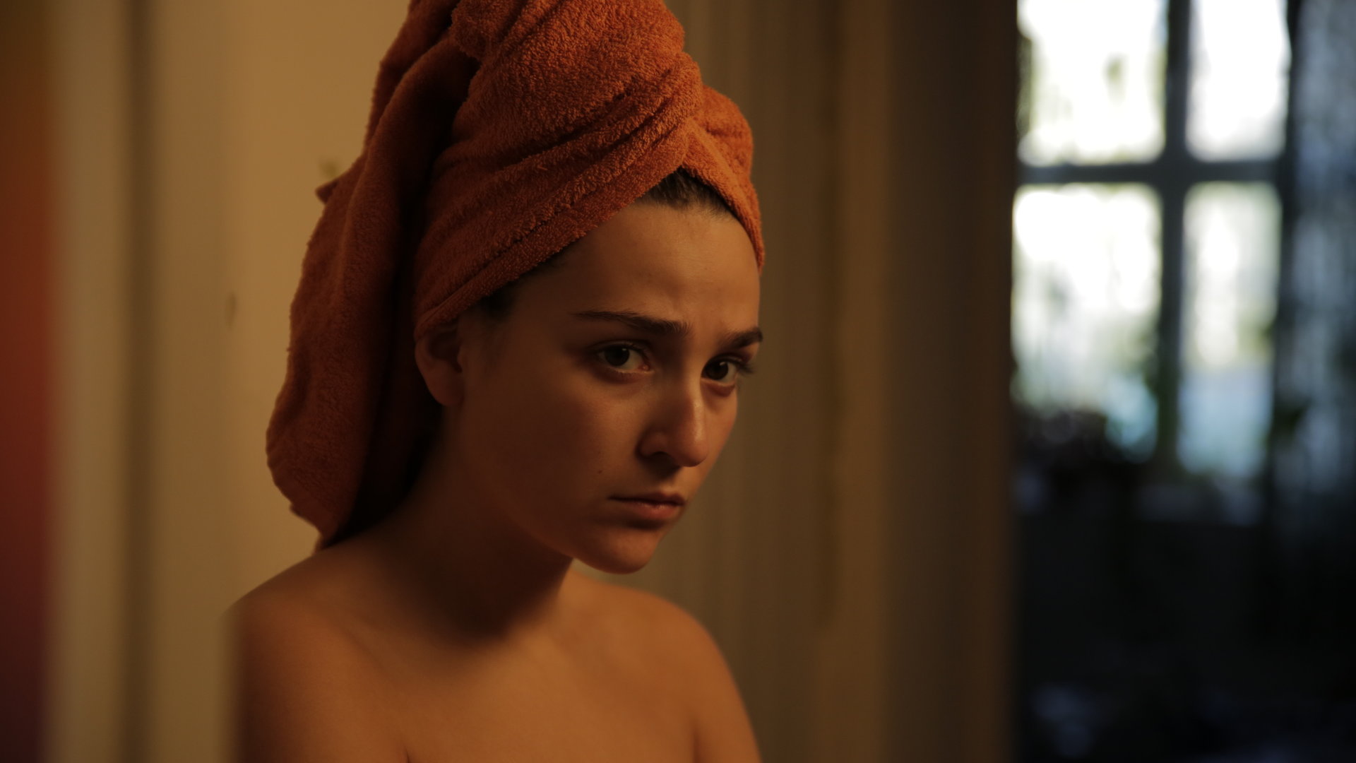 "About Saturday - Screw you guys I'm going home": Klara (Darin Hagi) steht mit einem Handtuch bekleidet in einem Flur und beobachtet etwas.