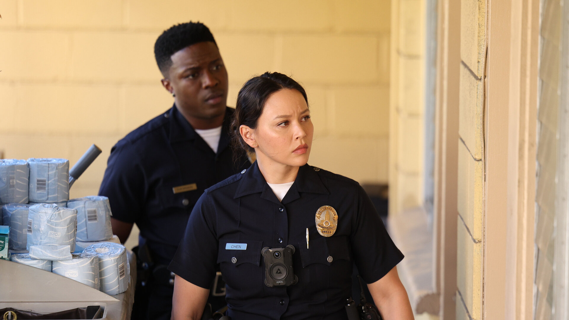 "The Rookie - Rückschlag": Officer Lucy Chen (Melissa O'Neil) und Aaron Thorsen (Tru Valentino) laufen konzentriert an der Hauswand eines Motels entlang.