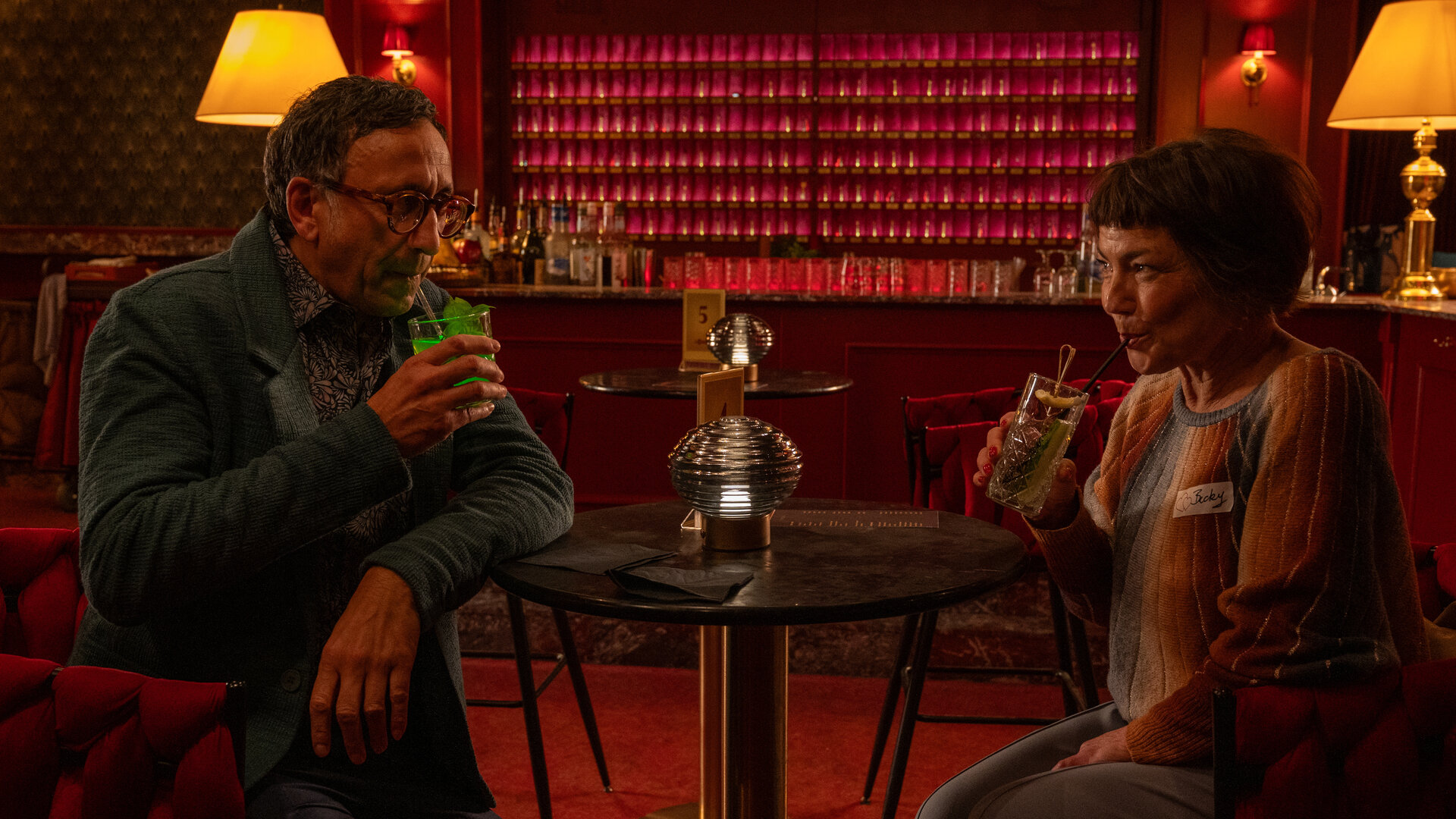 "SOKO Stuttgart - Speeddating": Der Leiter Der KTU Jan Arnaud (Mike Zaka Sommerfeldt) und Becky Rothe (Claudia Schmutzler) sitzen sich in einer Bar an einem Tisch gegenüber. Beide halten Drinks in der Hand, ziehen an ihren Strohhalmen und schauen sich dabei vertraut an.