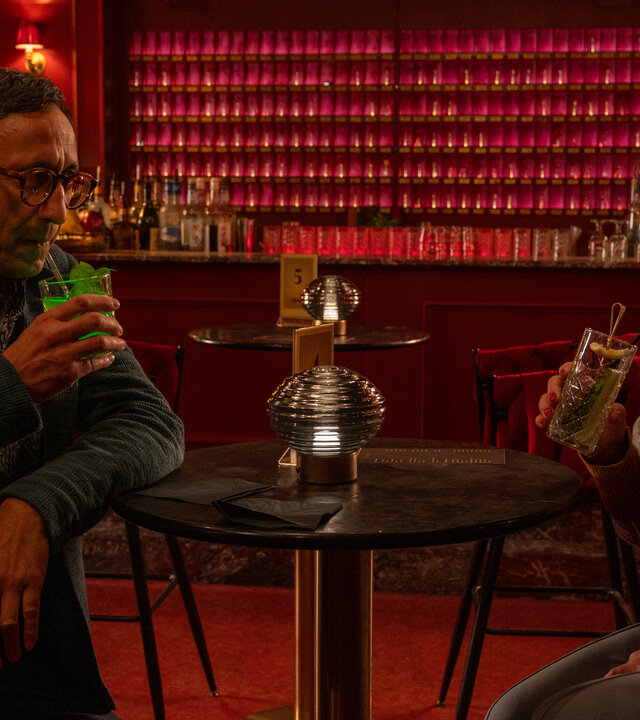 "SOKO Stuttgart - Speeddating": Der Leiter Der KTU Jan Arnaud (Mike Zaka Sommerfeldt) und Becky Rothe (Claudia Schmutzler) sitzen sich in einer Bar an einem Tisch gegenüber. Beide halten Drinks in der Hand, ziehen an ihren Strohhalmen und schauen sich dabei vertraut an.