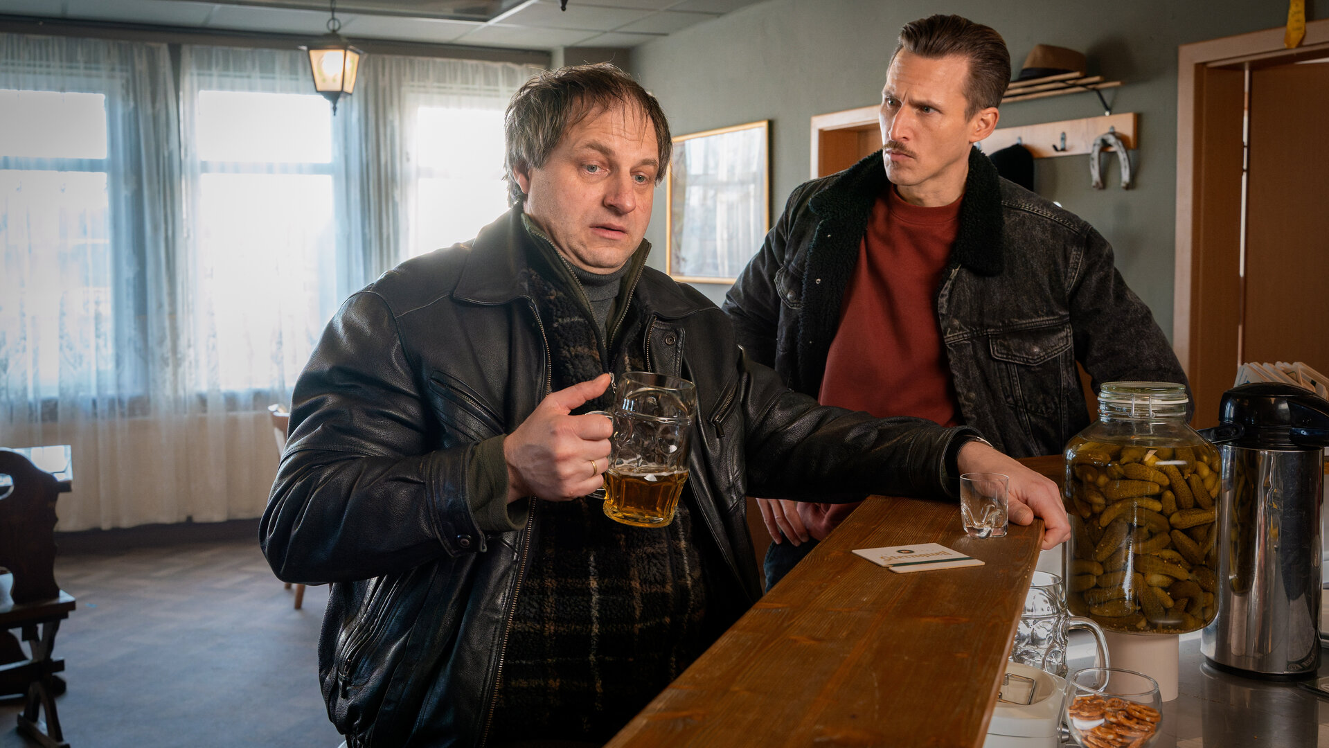 "SOKO Leipzig - Lucky": Uli (Stephan Möller-Titel) sitzt am Tresen einer Kneipe und hält einen Humpen Bier in der Hand. Moritz (Johannes Hendrik Langer) steht neben ihm und befragt ihn.