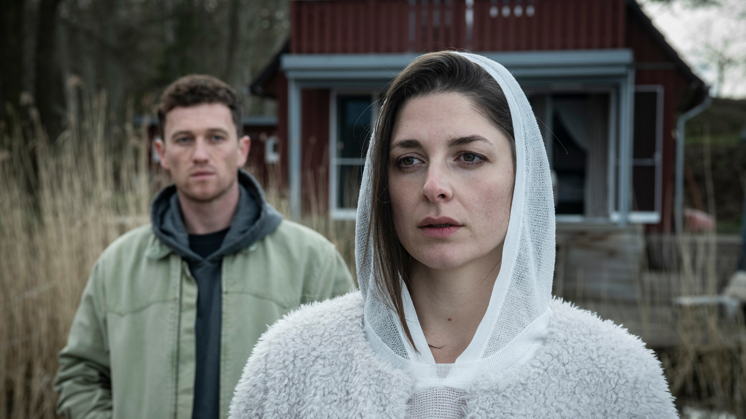 "Die Whistleblowerin": Galina Gromowa (Katharina Nesytowa) steht vor einem schwedischen Ferienhaus und schaut in die Ferne. Hinter ihr steht Tom Arndt (Artjom Gilz) und betrachtet sie.