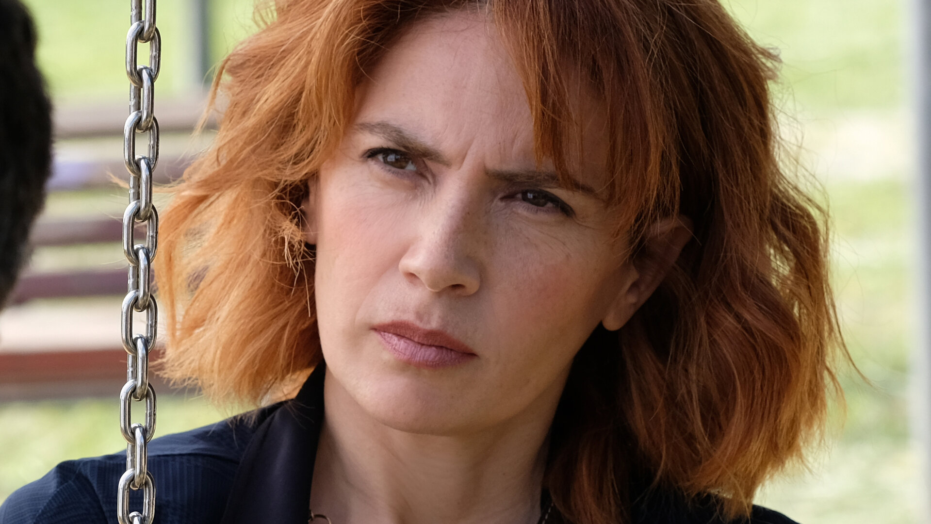 "Standing Tall - Kein Zufall": Nahaufnahme: Sara (Maya Sansa), die Stirn in Falten, blickt mit kritischem Blick Valerio (Alessandro Gassmann) an. Diese ist nur mit einem winzigen Teil des Hinterkopfs im Anschnitt abgebildet. Vor Sara hängt die Gliederkette einer Schaukel.