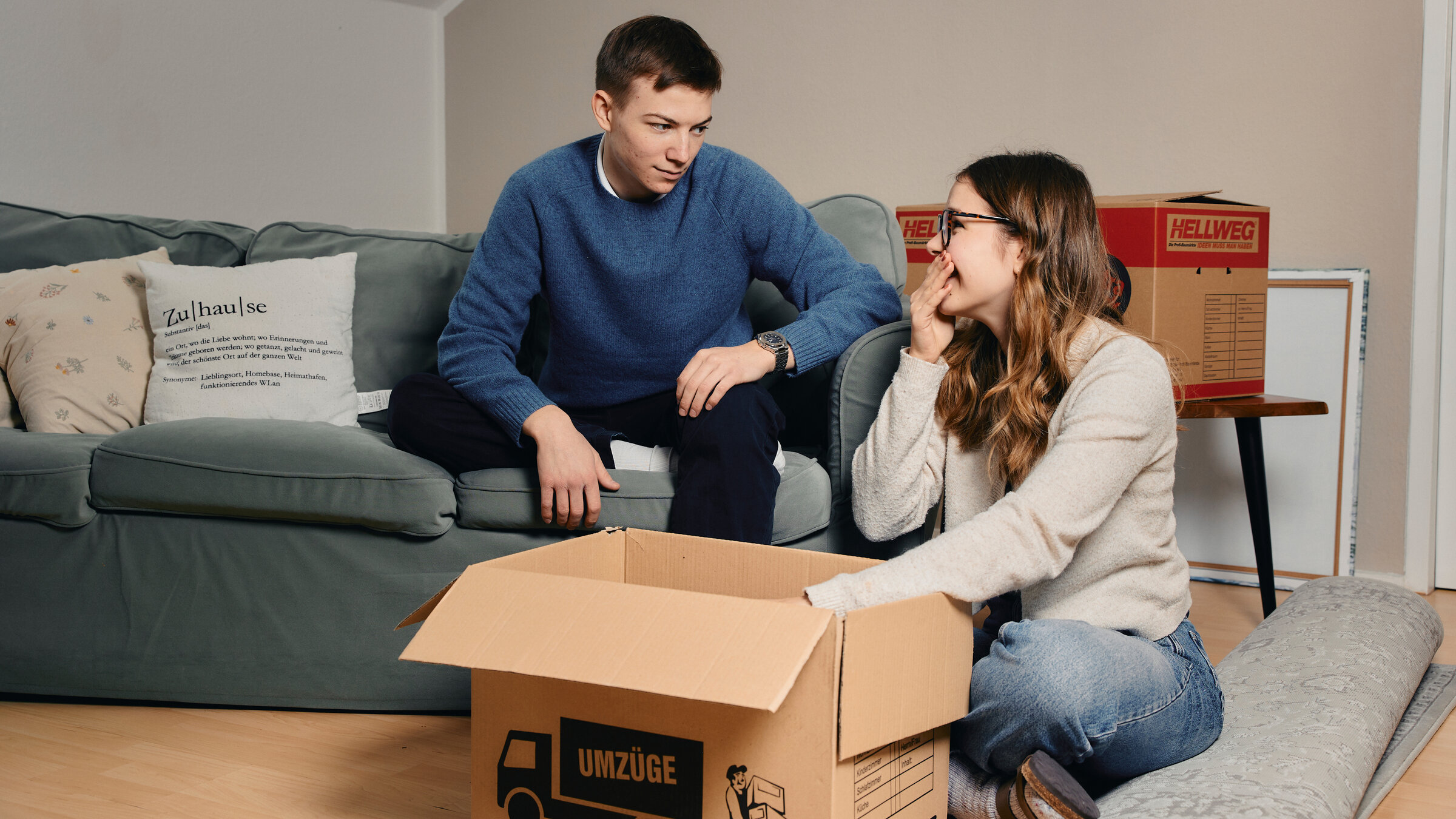 "37°: Paare, die zusammenziehen - Stresstest gemeinsame Wohnung": Stintje und Yuri sitzen vor Umzugskartons, er auf der Couch, sie auf dem Boden.
