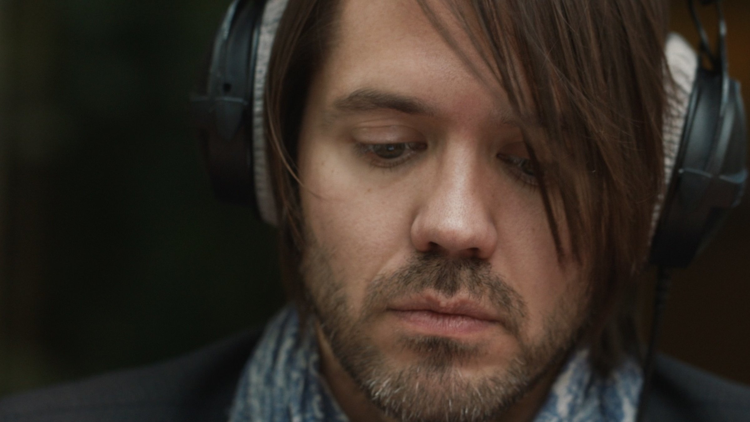 "Wie ein Fremder - Eine deutsche Popmusik-Geschichte - Ghost": Kopf eines jungen, bärtigen Mannes mit Kopfhörern in Großaufnahme.